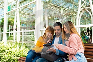 A photographer shows his work on his camera to two young girls sitting on a bench