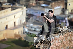 Photographer sitting on a rock high above the city blocks and removes Indian city