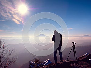 Photographer stay with camera ind hands at tripod on rock