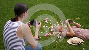 photographer takes pictures of a girl lying a beautiful woman in a green meadow, who holds a bouquet of peonies in front