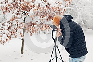 Photographer taking photos using professional digital camera on tripod in snowy winter park. Landscape pictures