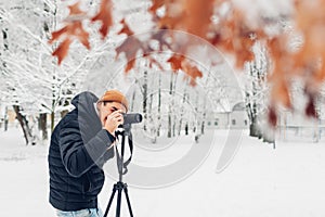 Photographer taking photos using professional digital camera on tripod in snowy winter park. Landscape pictures