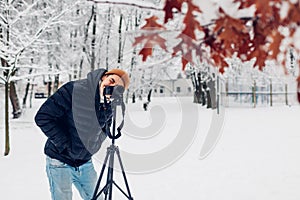 Photographer taking photos using professional digital camera on tripod in snowy winter park. Landscape pictures