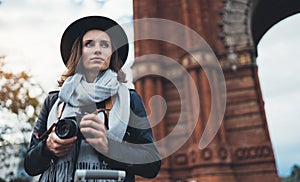 Photographer tourist with retro photo camera. Girl in hat travels in Triumphal arch Barcelona. Holiday concept in europe street