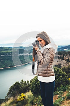 Photographer tourist traveler standing on green top on mountain holding in hands digital photo camera, hiker taking click photo