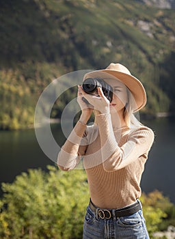 Photographer tourist traveler standing on green top on mountain holding in hands digital photo camera