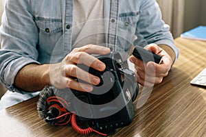 A photographer or videographer changing the battery of his camera. The camera has an external microphone for vlogs and videos on