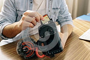A photographer or videographer changing the memory card of your camera. The camera has an external microphone for vlogs and videos