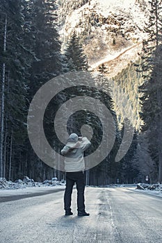 Photographer walks down a road in the winter with his camera.