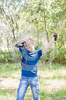 Photographer wearing blue t-shirt working outdoors. Summer day. Young man with a DSLR camera and light equipment in hands