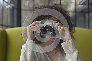 Curly haired photographer woman holding her camera in a cafe and shooting