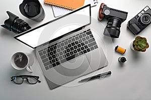 Photographer workspace with laptop computer, camera, coffee cup and glasses on white table.