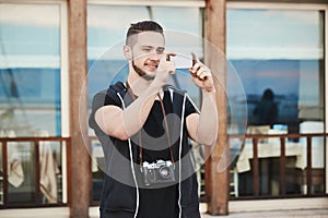 Photographers love this smartphone. Outdoor portrait of handsome european photographer in trendy clothes taking photo on