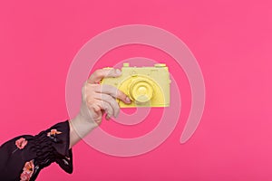 Photographing and vintage concept - female hand with yellow retro camera on pink background with copy space