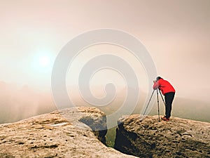 Photographr looking into viewfinder of dslr digital camera stand on tripod. Artist photographing mountain and cloudy landscape