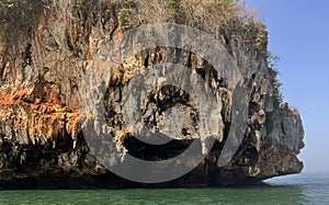 a photography of a boat is in the water near a rock formation, drop - off of a cliff into the ocean with a boat in the water