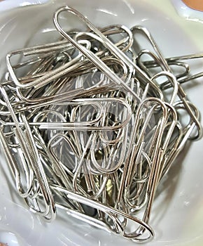 a photography of a bowl of silver colored paper clips, safety pin in a bowl of silver colored metal