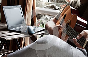 photography of boy learning to play the guitar with the computer, online classes.