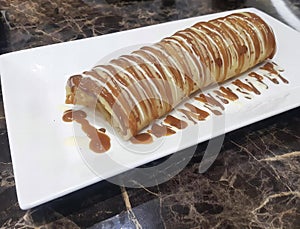 a photography of a pastry with caramel sauce on a white plate, there is a long pastry with caramel sauce on a plate