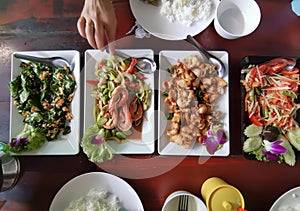 a photography of a table with plates of food and bowls of rice, plate of food on a table with a person reaching for a fork