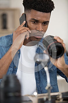 photography technician examining camera lens and talking on smartphone photo