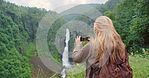 Photography, tourist or woman taking pictures in nature for travel, adventure or sightseeing scenery. Waterfall, lady or