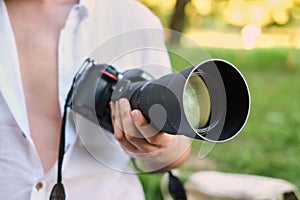 Photography or traveler Concept.The photographer hold DSRL camera in his hands with a large lens on the background of nature and s