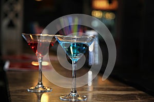 Photography of two martini glasses filled with a colored cocktails standing on the bar counter