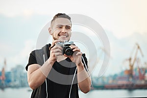 Photojournalist likes his work. Portrait of happy pleased handsome photographer smiling broadly while looking aside and