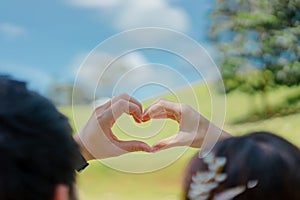 Photos from the back of a man and a woman raise a hand above the head and pose in heart shape.