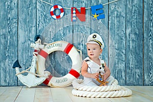 Photoshoot for a boy of one year. Little sea captain, sailor on toy ship with steering wheel. Sea anchor and lifebuoy on gray