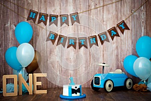 Photoshoot crush smashcake for a little boy gentleman. Decorated photozone with a wooden retro car and helium balloons. Happy