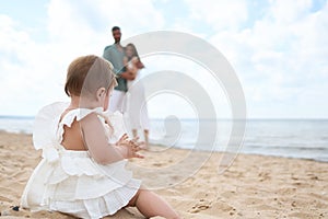 Photoshoot of happy parents admiring their 1 year old girl playing with sand on the beach