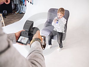 Photographer man photographs a little boy in a white shirt on a white background.