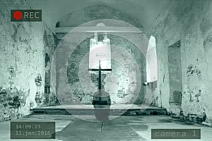 A Photoshop of a CCTV image of a hooded ghost kneeling next to a cross in a disused church.