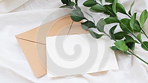 Photostock wedding styled composition. Feminine envelope mockup scene with ruscus leaves, silk ribbon, blank greeting card, on cre