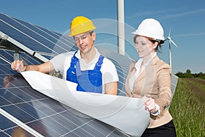 Photovoltaic engineers with construction plan at solar panels