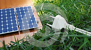 Photovoltaic solar panel next to a plug wire on grass background