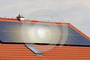 Photovoltaic or solar panels on roof of the house at sunset. Red roof with ecological solar system during the summer day. Clouds