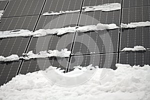 Photovoltaic solar panels on a roof partly covered with snow [