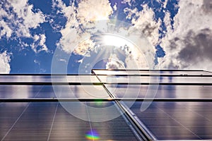 A photovoltaic system on a roof backlit with sun and clouds