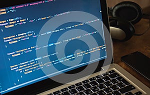 Php code on laptop`s display with cellphone and earphones on working place