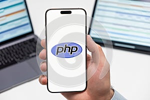 PHP logo on the screen of smartphone in mans hand on the workplace background