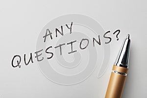 Phrase ANY QUESTIONS and pen on white paper