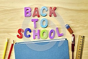 the phrase back to school is laid out in multicolored letters on the table a fountain pen a book a ruler a pencil next