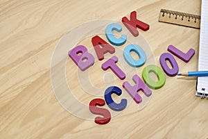 the phrase back to school is laid out in multicolored letters on the table next to a pencil ruler and a notebook with