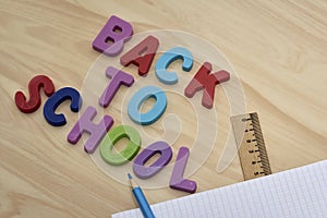 the phrase back to school is laid out in multicolored letters on the table next to a pencil ruler and a notebook with