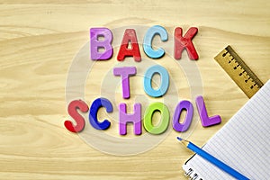 the phrase back to school is laid out in multicolored letters on the table next to a pencil ruler and a notebook with