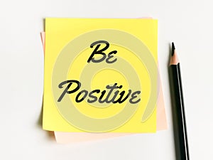 Phrase Be Positive written on sticky note with a pencil.