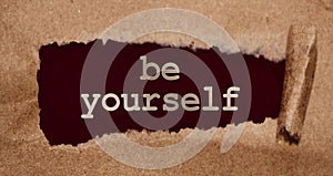 The phrase Be yourself typed on dark red paper with hite ink through torn paper, Motivation coaching career business concept